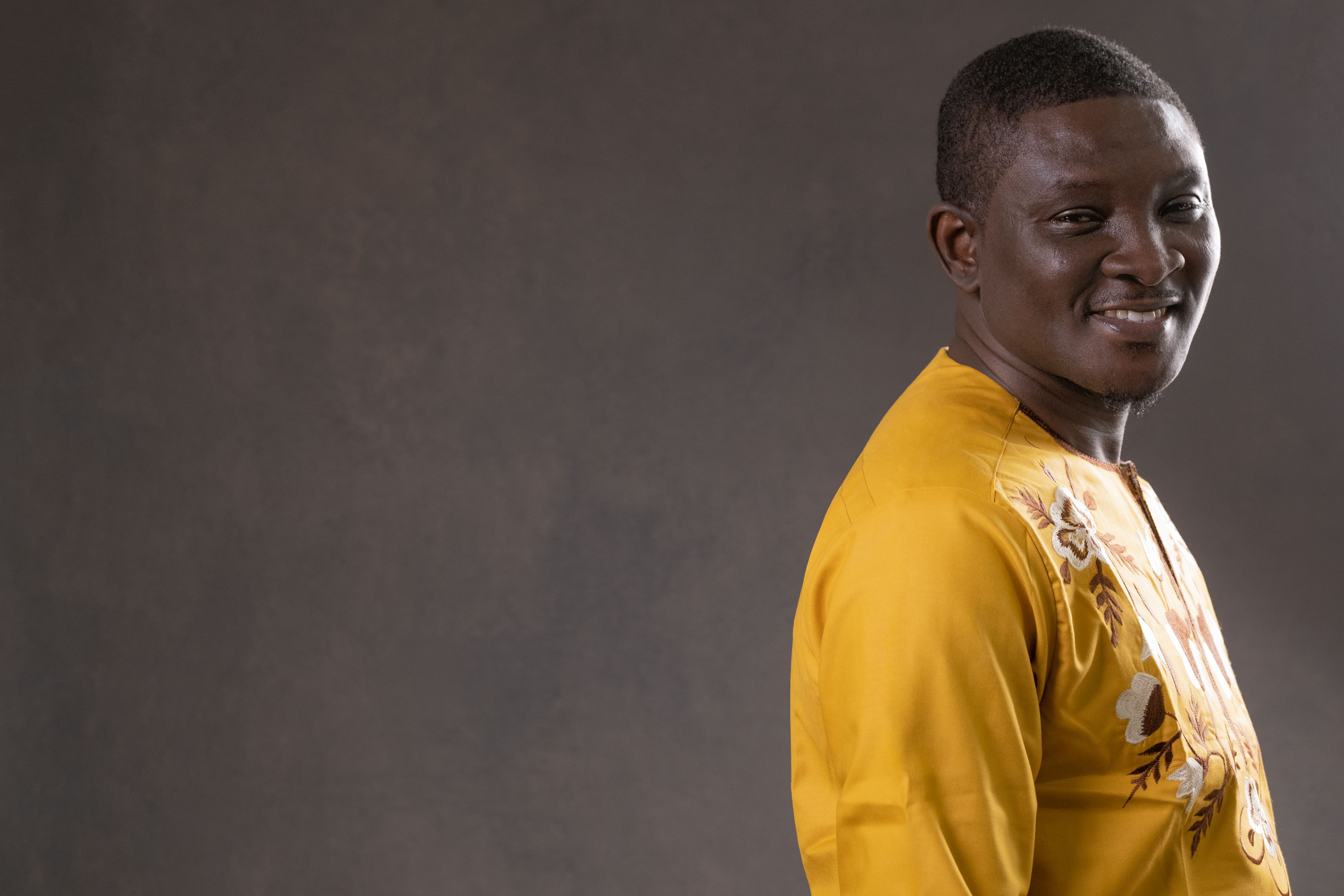 Paul Ugbede in a vibrant yellow traditional outfit, looking over his shoulder