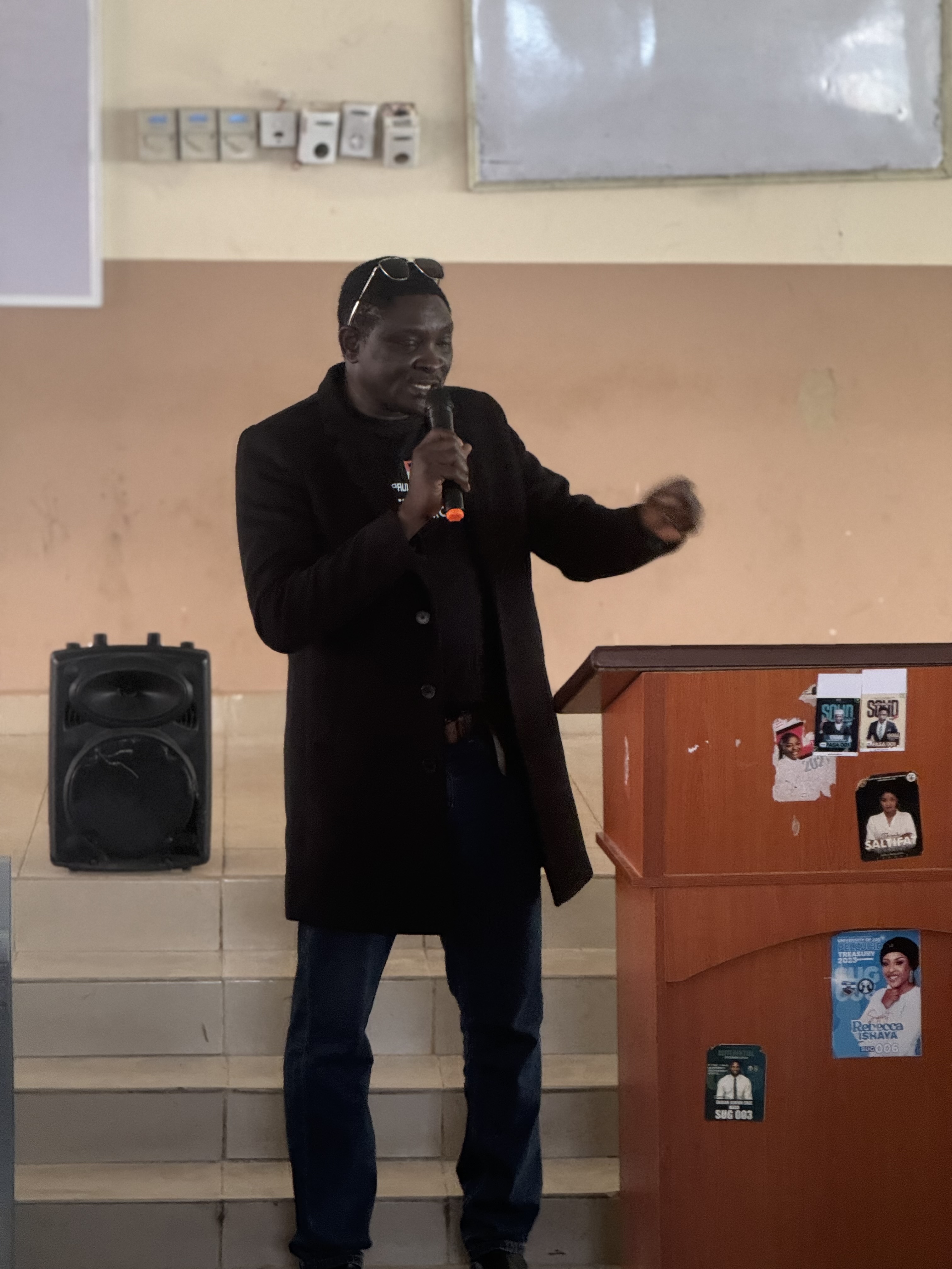 Paul Ugbede speaking with a microphone at a workshop session
